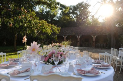 Grande table dressée avec vaisselle élégante, pains individuels et décoration florale, sous une terrasse en bois ouverte sur…