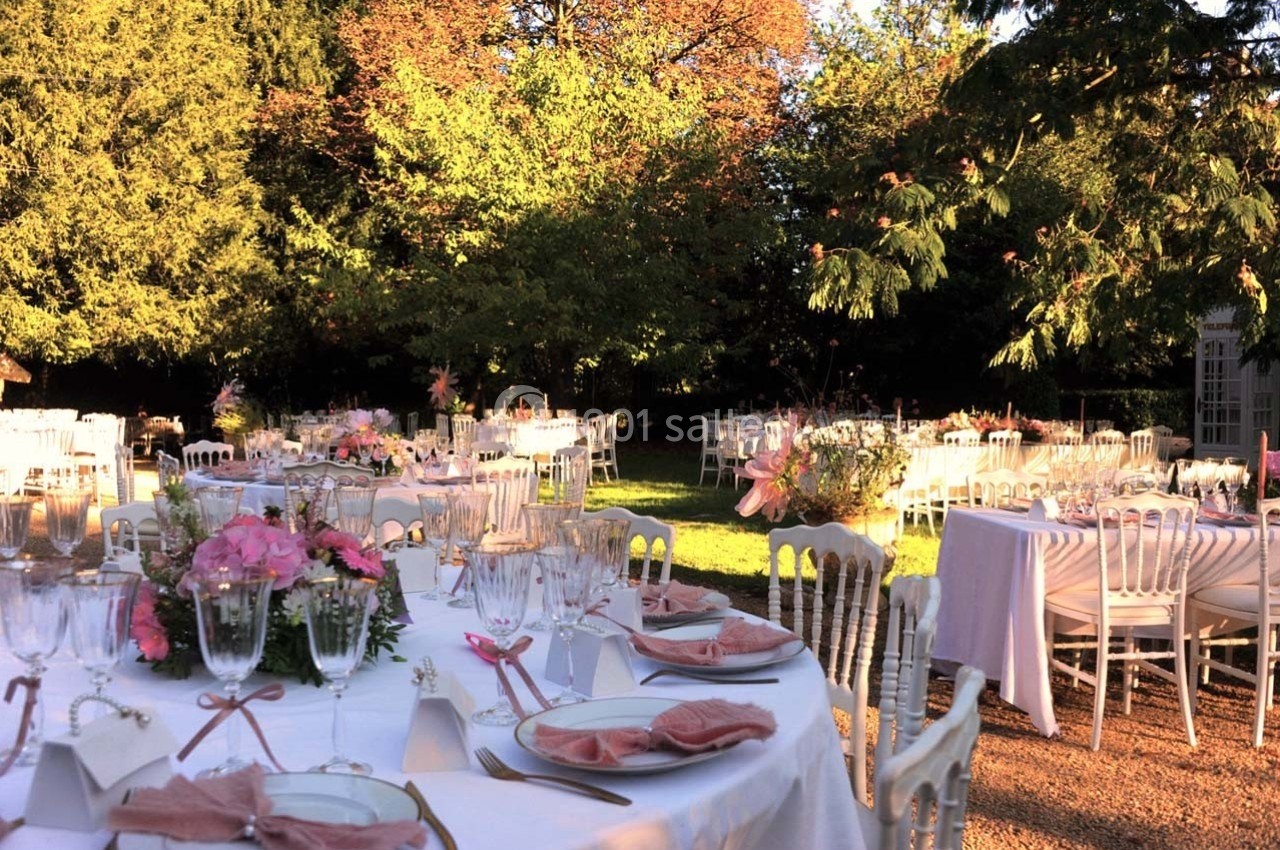 Tables élégamment dressées en extérieur, entourées de verdure, avec des décorations florales et une lumière douce.