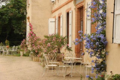 Grande table dressée avec vaisselle élégante, pains individuels et décoration florale, sous une terrasse en bois ouverte sur…
