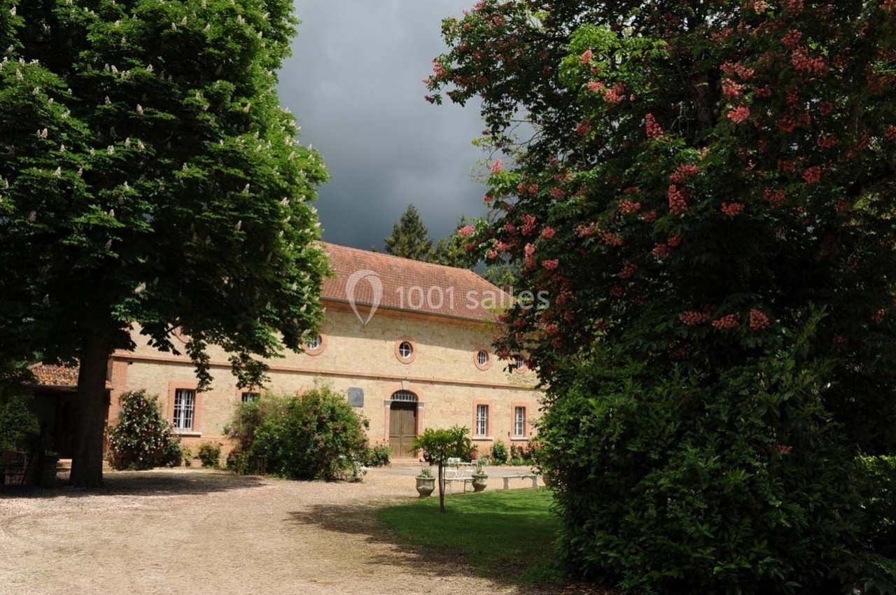 Bâtiment en briques entouré d'arbres et de végétation sous un ciel nuageux.