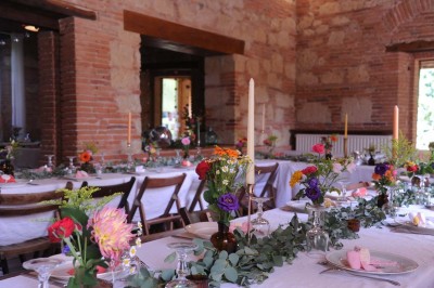 Grande table dressée avec vaisselle élégante, pains individuels et décoration florale, sous une terrasse en bois ouverte sur…