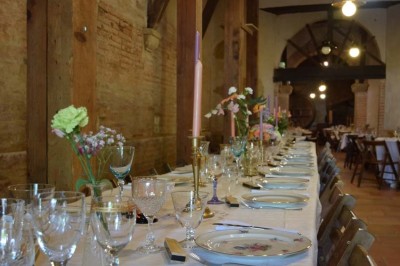 Grande table dressée avec vaisselle élégante, pains individuels et décoration florale, sous une terrasse en bois ouverte sur…