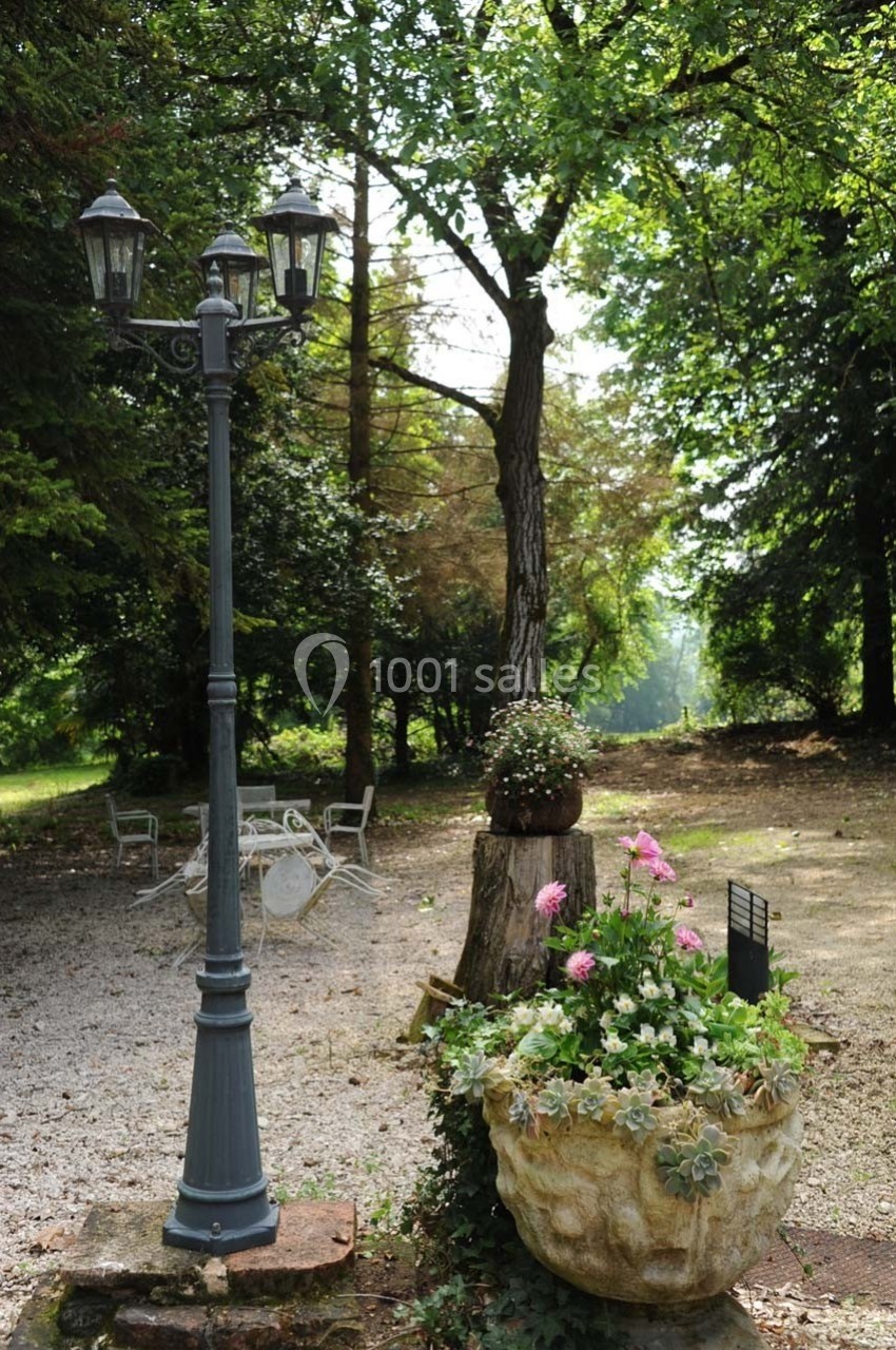Lampadaire en fer forgé près d'une table de jardin, entouré de plantes et d'arbres dans un cadre boisé.