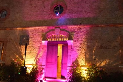 Grande table dressée avec vaisselle élégante, pains individuels et décoration florale, sous une terrasse en bois ouverte sur…