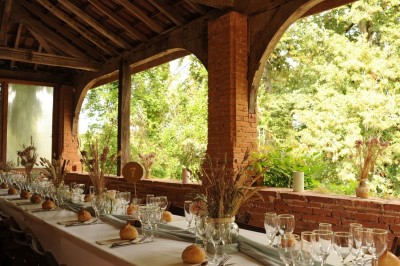 Grande table dressée avec vaisselle élégante, pains individuels et décoration florale, sous une terrasse en bois ouverte sur…
