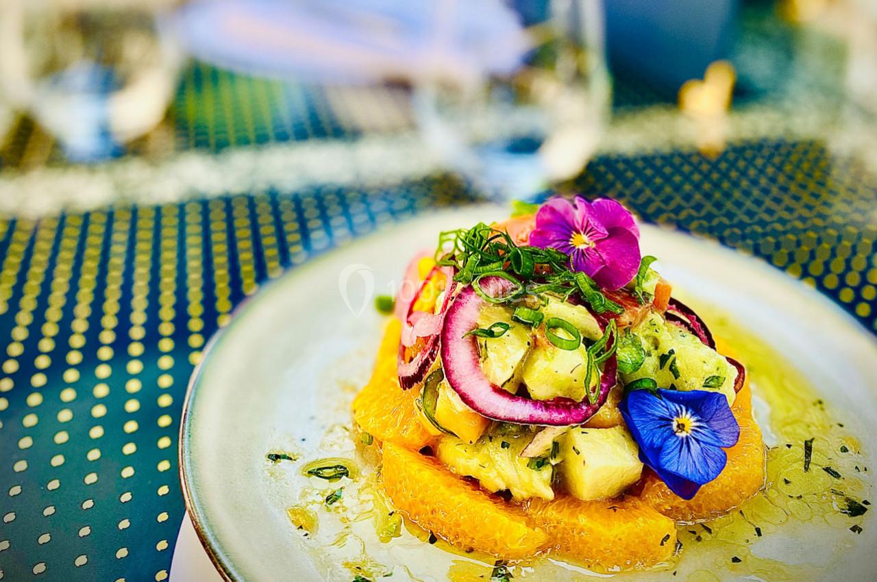 Assiette de salade colorée avec fruits exotiques, fleurs comestibles et herbes fraîches sur une table extérieure.