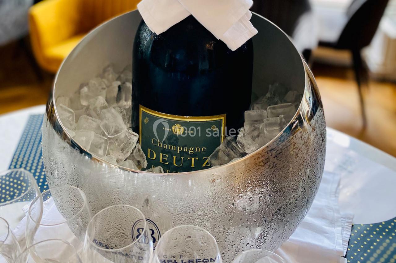 Bouteille de champagne Deutz placée dans un seau argenté rempli de glaçons, entourée de verres vides.