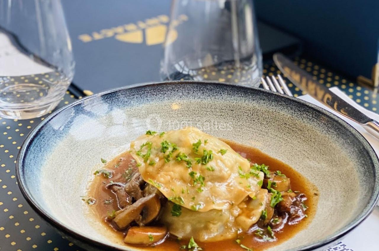 Assiette de ravioles garnies, servies avec une sauce brune, des champignons et parsemées de persil frais.