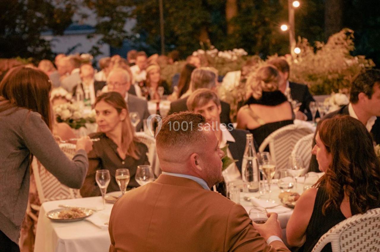 Des convives assis autour de tables décorées, partageant un repas en extérieur dans une ambiance chaleureuse en soirée.