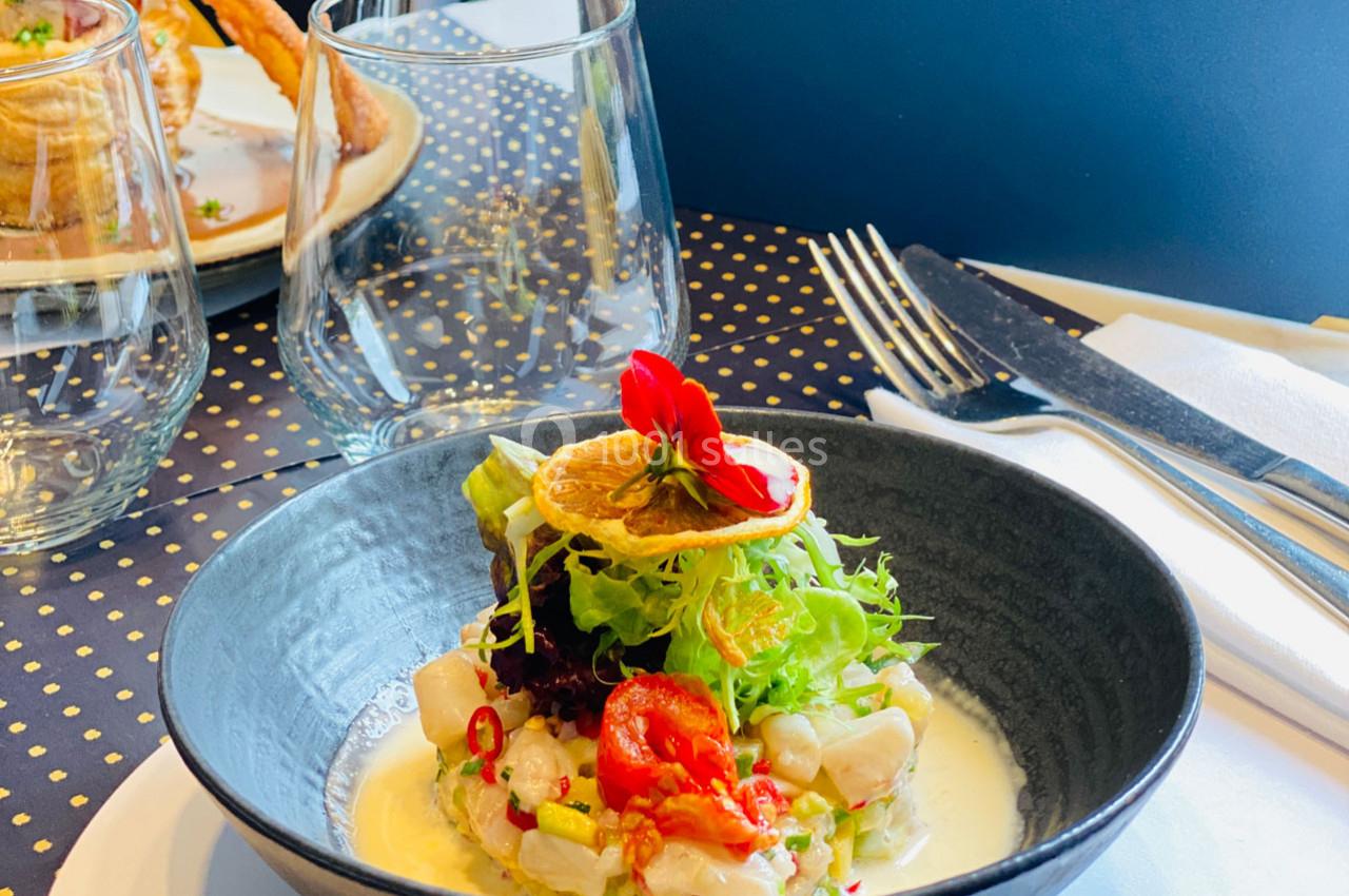 Plat de ceviche servi dans un bol noir, garni de salade, rondelle de citron séché et fleurs comestibles.