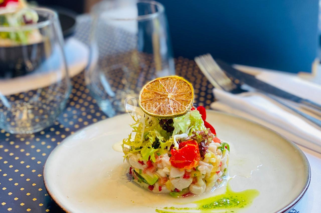 Assiette de ceviche dressée avec des légumes, herbes fraîches et une rondelle de citron séché, servie sur une table élégante.