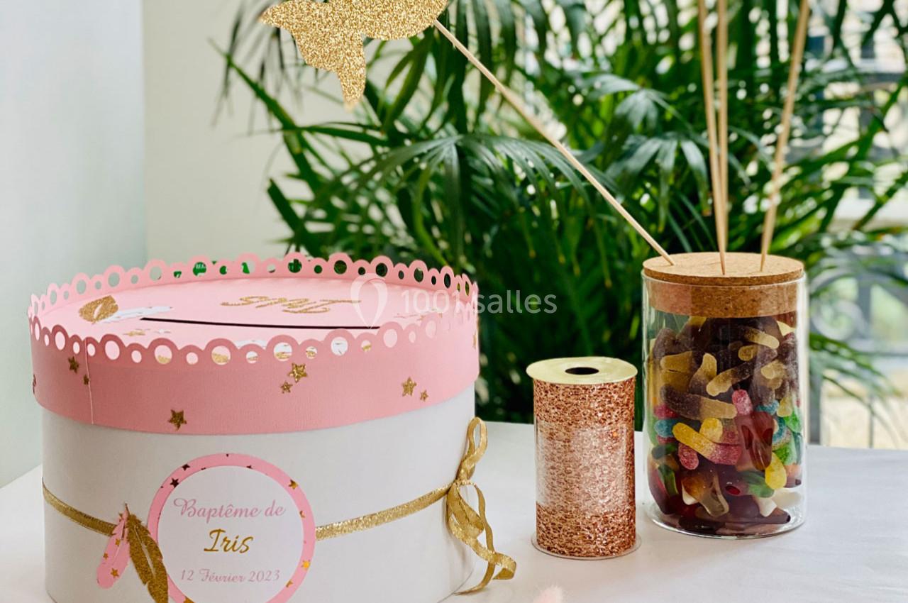 Boîte décorative rose et blanche pour un baptême, accompagnée d'un pot de bonbons et d'éléments dorés sur une table.