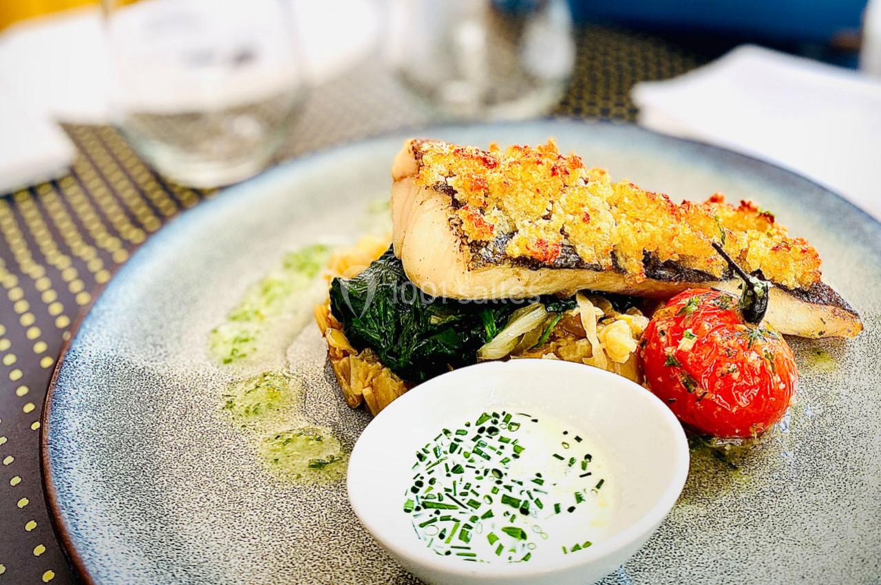 Plat de poisson grillé avec croûte dorée, légumes sautés, tomate rôtie et sauce blanche garnie de ciboulette.