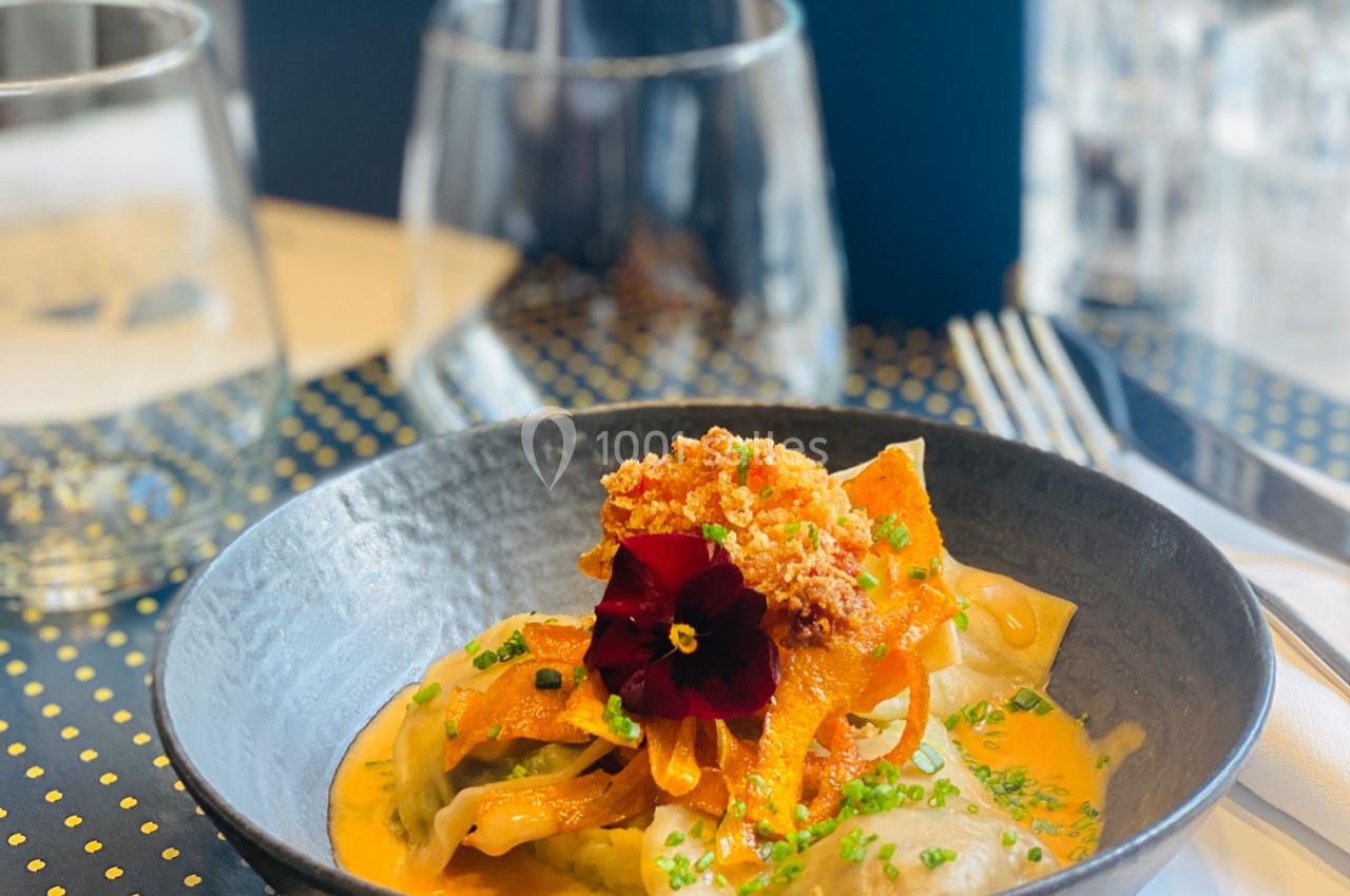 Assiette de ravioles garnies de légumes, sauce crémeuse orange, décorée d'une fleur comestible et de ciboulette.