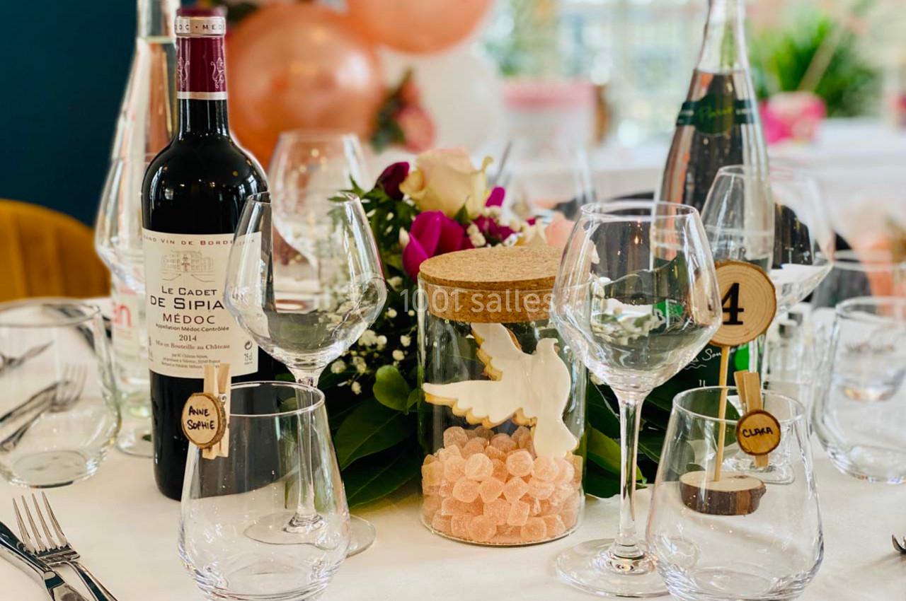 Table décorée avec des verres, une bouteille de vin, des fleurs, des bonbons et des ballons en arrière-plan.