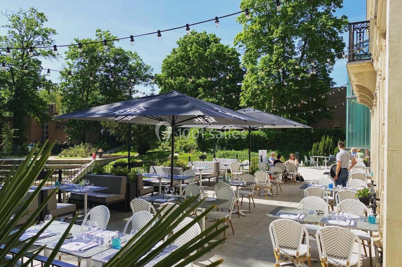 Terrasse extérieure d'un restaurant avec tables dressées, parasols noirs et vue sur un jardin verdoyant par une journée…