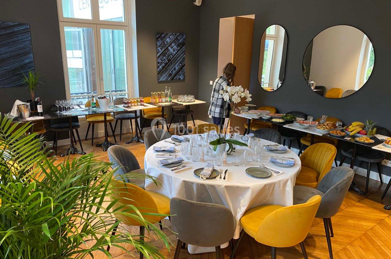 Salle élégante avec une table ronde dressée, chaises colorées, buffet varié et décor moderne.