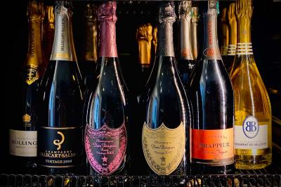 Bouteilles de champagne variées alignées sur une étagère réfrigérée, étiquettes visibles.