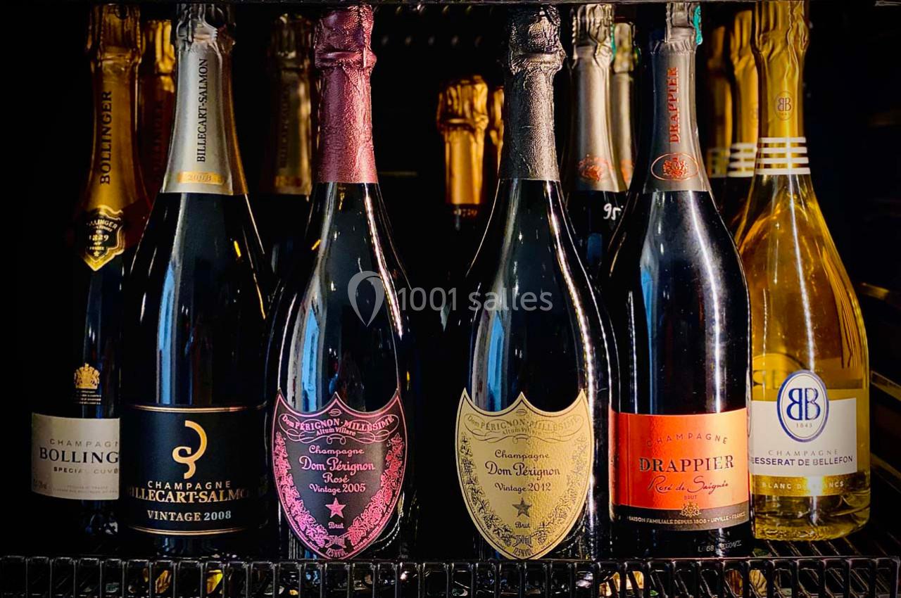 Bouteilles de champagne variées alignées sur une étagère réfrigérée, étiquettes visibles.