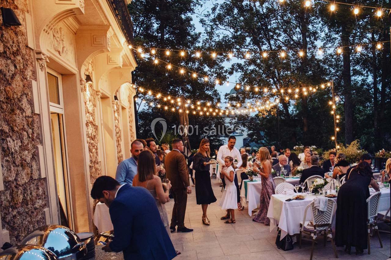 Dîner en plein air avec des invités discutant sous des guirlandes lumineuses, près d'un bâtiment en pierre.