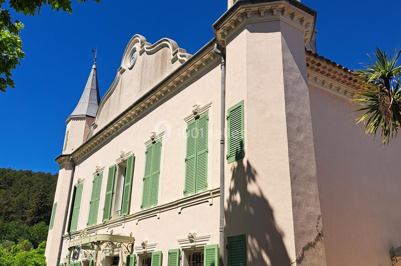 Façade d'une maison ancienne avec volets verts, deux tours et un ciel bleu dégagé en arrière-plan.