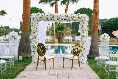 Décoration de table de mariage en extérieur avec chandeliers en verre, fleurs blanches et chaises alignées sur une pelouse.