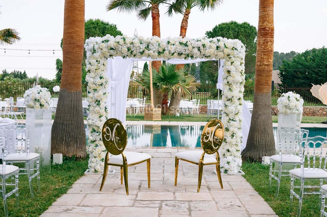 Arche de mariage ornée de fleurs blanches, entourée de chaises et située près d'une piscine dans un jardin.