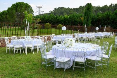 Décoration de table de mariage en extérieur avec chandeliers en verre, fleurs blanches et chaises alignées sur une pelouse.
