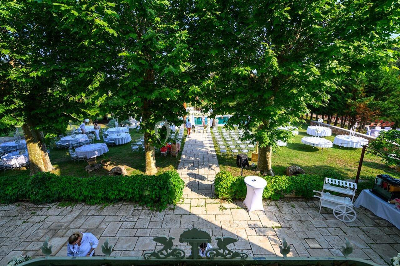 Jardin aménagé pour un événement avec tables dressées, allée centrale pavée et piscine en arrière-plan.
