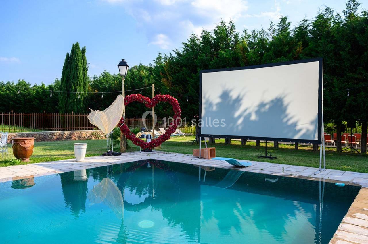 Écran de projection en plein air près d'une piscine, décoré d'un cœur en fleurs rouges et d'une lampe vintage.