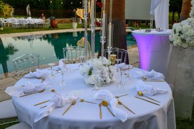 Décoration de table de mariage en extérieur avec chandeliers en verre, fleurs blanches et chaises alignées sur une pelouse.