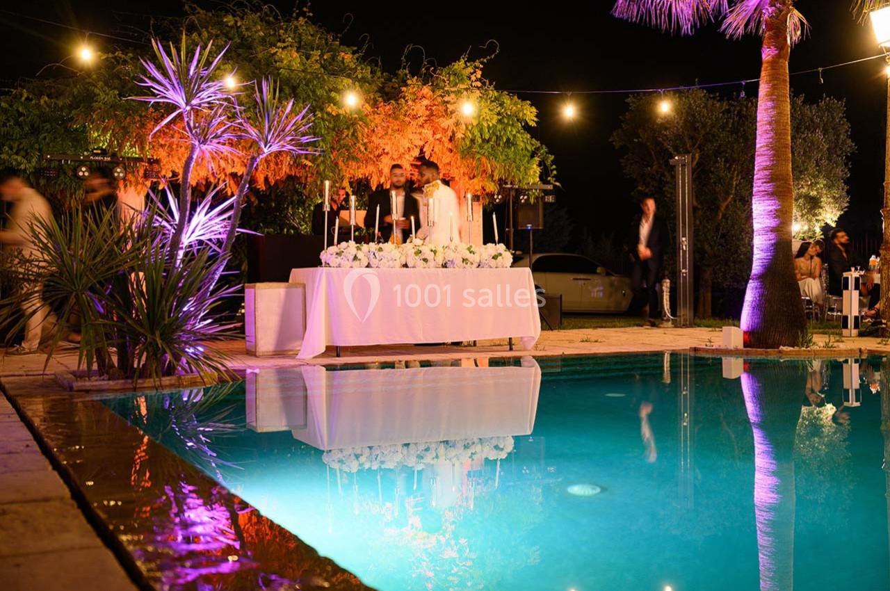 Table décorée avec des bougies près d'une piscine éclairée, entourée de végétation et d'éclairages nocturnes.