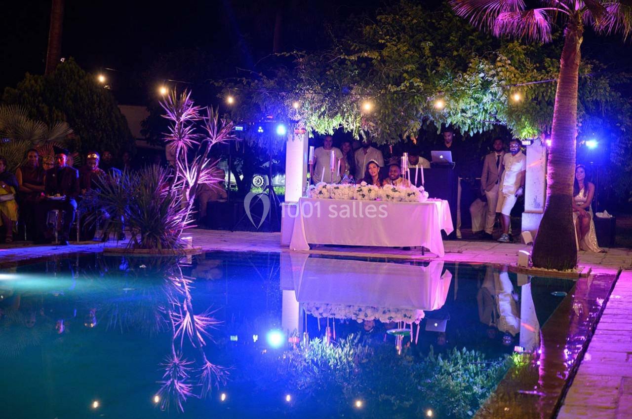 Un mariage en soirée près d'une piscine éclairée, avec des invités et une table décorée de fleurs blanches.