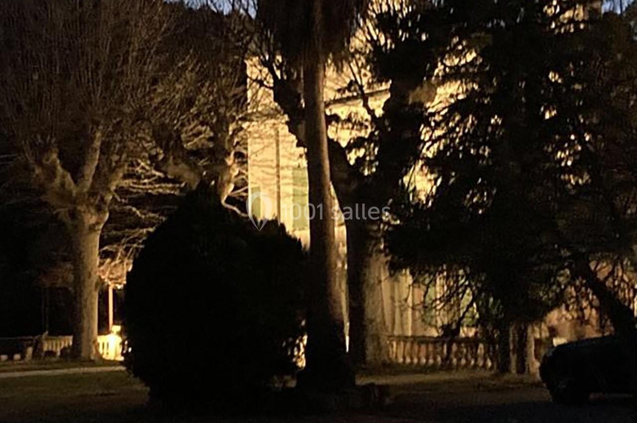 Façade d'un bâtiment éclairé la nuit, entourée d'arbres et de végétation sombre.