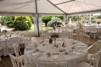 Décoration de table de mariage en extérieur avec chandeliers en verre, fleurs blanches et chaises alignées sur une pelouse.