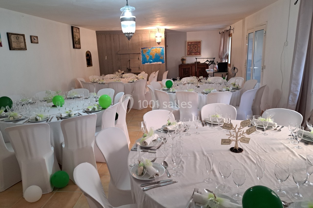 Salle décorée pour un événement, avec tables rondes dressées, nappes blanches, ballons verts et centre de table élégant.