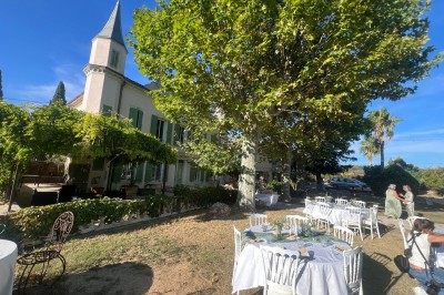 Tables dressées en extérieur avec nappes blanches, entourées de chaises, près d'une piscine et de palmiers sous un ciel bleu.