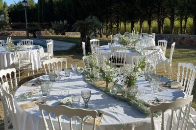 Tables dressées en extérieur avec nappes blanches, entourées de chaises, près d'une piscine et de palmiers sous un ciel bleu.