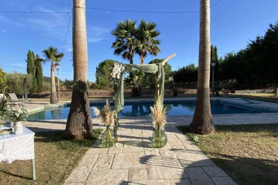 Tables dressées en extérieur avec nappes blanches, entourées de chaises, près d'une piscine et de palmiers sous un ciel bleu.
