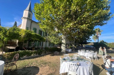 Tables dressées en extérieur avec nappes blanches, entourées de chaises, près d'une piscine et de palmiers sous un ciel bleu.