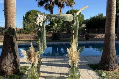 Tables dressées en extérieur avec nappes blanches, entourées de chaises, près d'une piscine et de palmiers sous un ciel bleu.