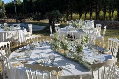Tables dressées en extérieur avec nappes blanches, entourées de chaises, près d'une piscine et de palmiers sous un ciel bleu.