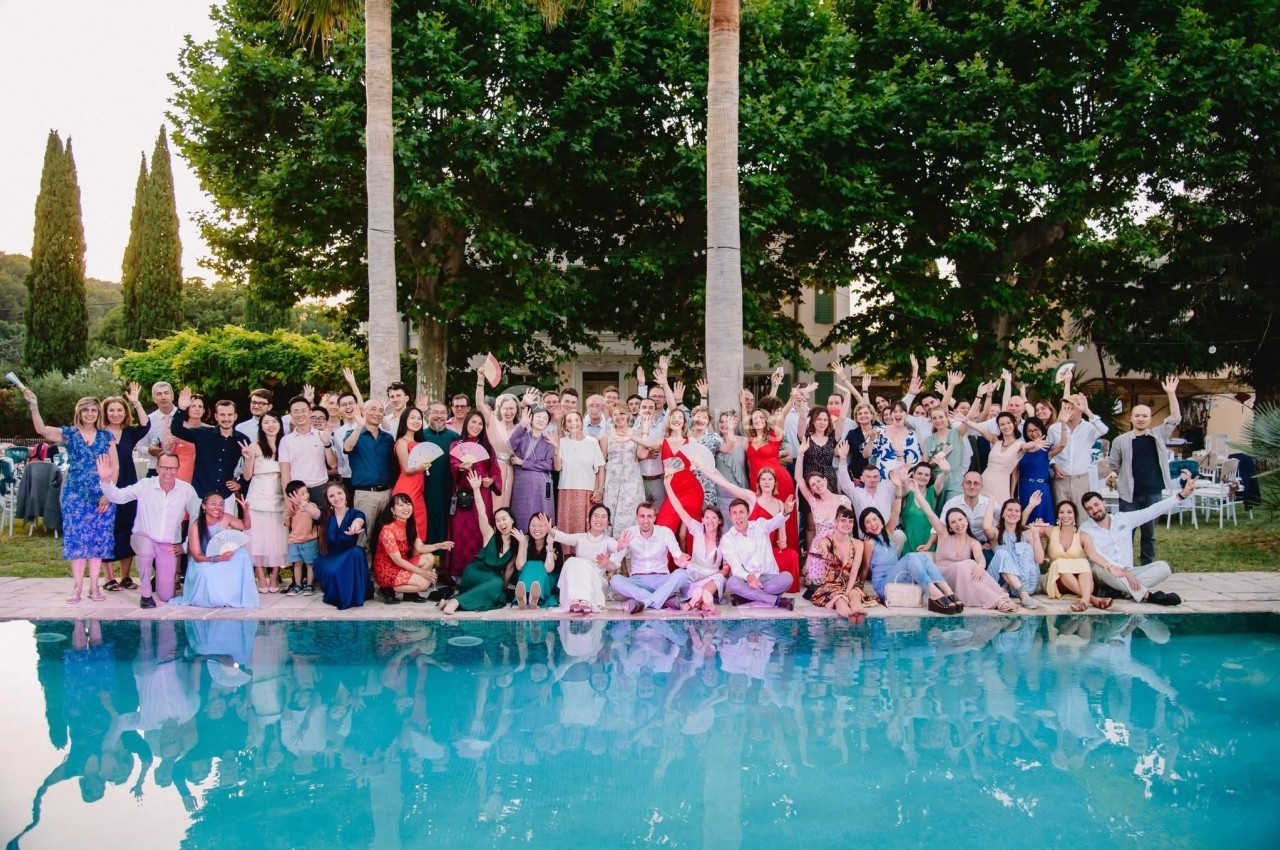 Un grand groupe de personnes pose joyeusement devant une piscine, entouré de végétation et d'arbres.