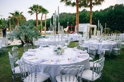 Décoration de table de mariage en extérieur avec chandeliers en verre, fleurs blanches et chaises alignées sur une pelouse.