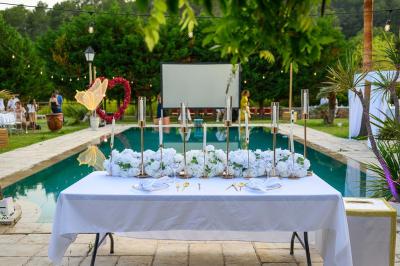 Décoration de table de mariage en extérieur avec chandeliers en verre, fleurs blanches et chaises alignées sur une pelouse.