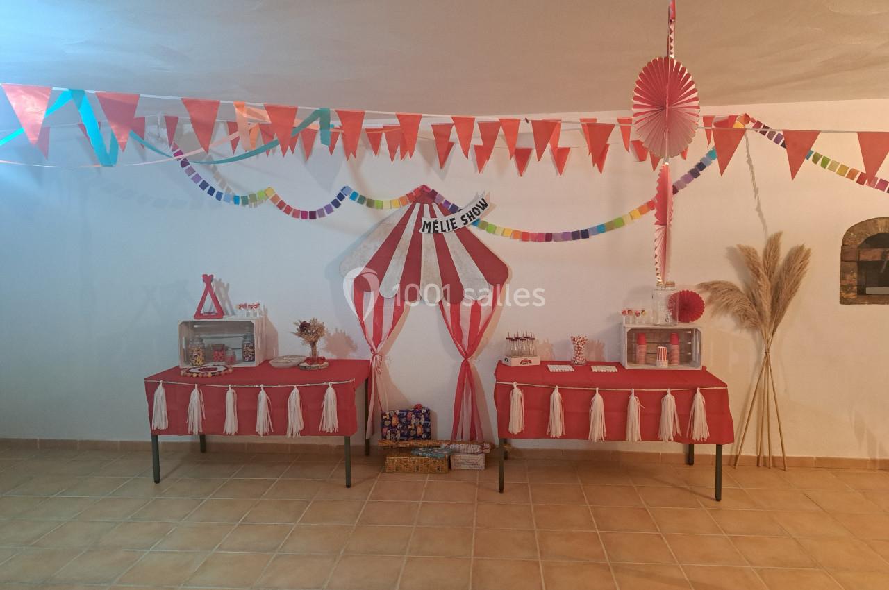 Décoration festive sur le thème du cirque avec guirlandes, tables rouges et blanches, et accessoires colorés.
