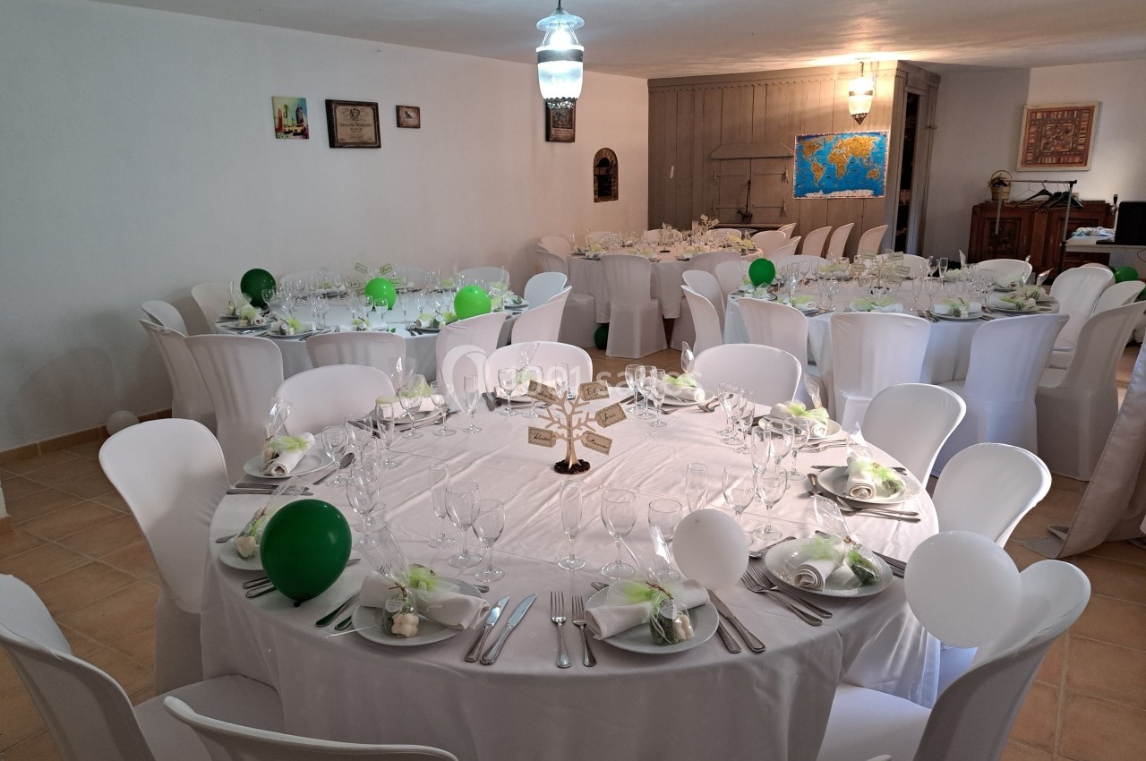 Salle décorée pour un événement avec des tables rondes dressées, nappes blanches et ballons verts et blancs.