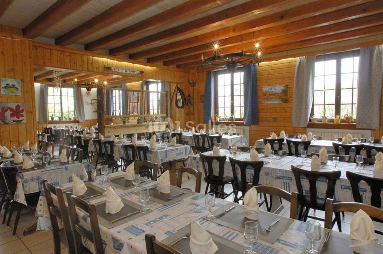 Salle de restaurant lumineuse avec tables dressées, nappes à motifs bleus et poutres apparentes au plafond.