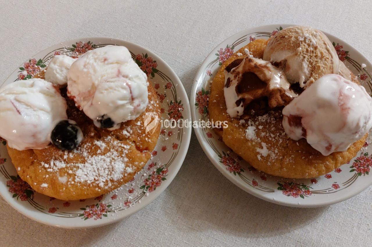 Deux assiettes avec des beignets saupoudrés de sucre glace, garnis de boules de glace et de fruits rouges.