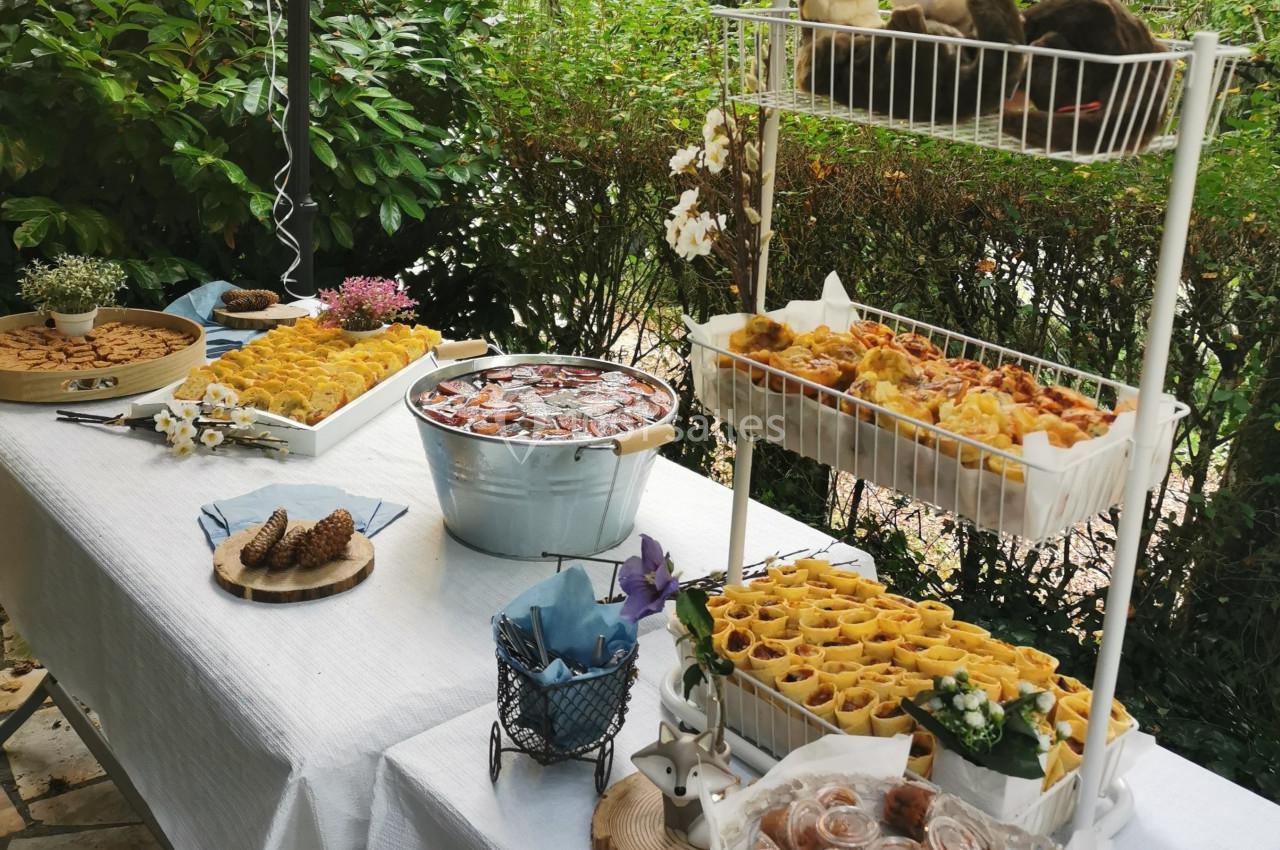 Table extérieure dressée avec des plats variés, dont des feuilletés, biscuits et une boisson dans un seau en métal.